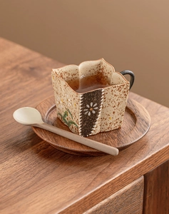 Close-up of a rustic ceramic tea cup with hand-painted patterns on a wooden saucer with spoon