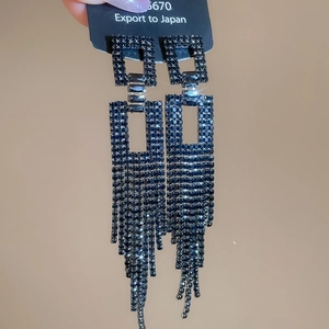 Détail de boucles d'oreilles noires à pampilles longues avec éléments carrés et strass