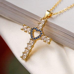 Gros plan d'un pendentif croix dorée avec pierres de cœur bleues et zircons blancs