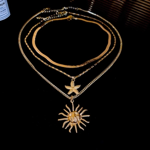 Close-up of triple-layered gold necklaces with starfish and sun pendants on black glass