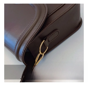 Macro detail of the premium golden metal hook on dark brown leather shoulder bag