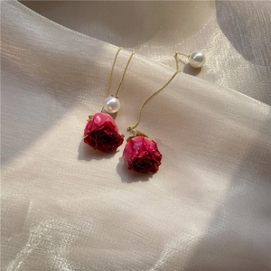 Macro shot of long red rose tassel earrings with pearls on champagne silk background