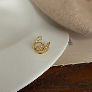 Detail of a gold layered ear cuff with white zircons on a white ceramic plate