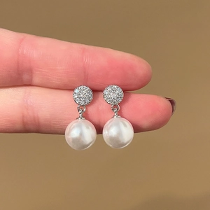 Close-up of sparkling zircon and white pearl drop earrings held against a neutral background