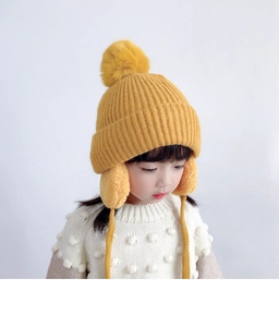 Close-up of ginger yellow knit kids hat featuring pom-pom and earflaps with soft texture