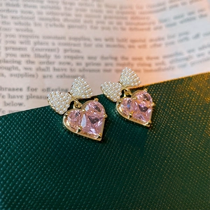 Detail of pink heart crystal earrings with pearl bow accents on a green leather surface