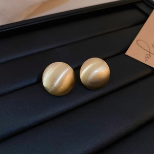 Close-up of matte gold hemispherical earrings with brushed metal texture on black leather