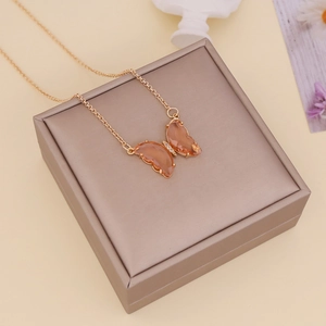 Detail of orange butterfly glass pendant on gold chain resting on beige jewelry box