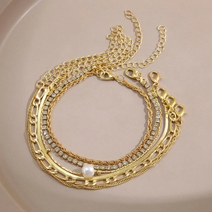 Close-up of gold layered bracelets featuring snake chain, rhinestones, and pearl charms