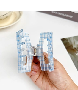 Blue and white checkered acrylic claw clip held by hand against a desk background