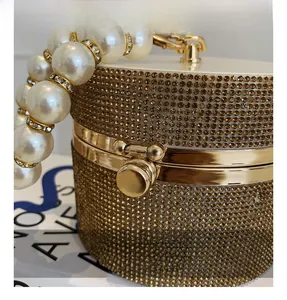 Detail of the golden rhinestone cylinder bag with pearl handle and metal clasp closure