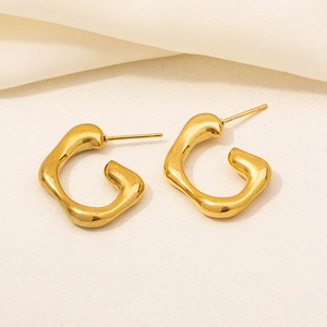 Macro shot of gold-plated stainless steel C-shape earrings on textured beige cloth