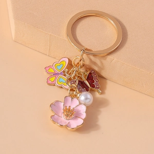 Floral butterfly keychain with pink sakura flower, pearl, and enamel accents on gold ring