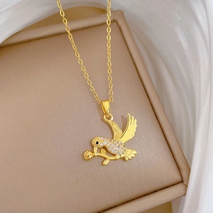 Close-up of golden swallow necklace with white crystals resting on a silk velvet box