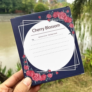 Close-up of a navy blue square gift box with red floral patterns in a natural setting