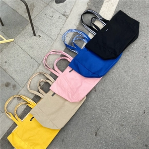 Flat lay of colorful canvas tote bags with plaid handles in five vibrant colors