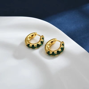 Macro detail of gold C-shaped earrings with inlaid emerald green zircon stones on fabric