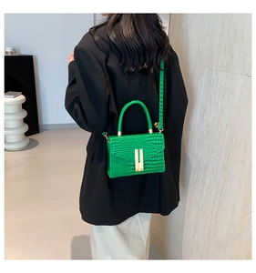 Close-up of green crocodile texture handbag with gold buckle shown on shoulder