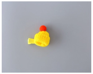 Close-up of yellow knitted mini hat hair clip with orange pompom on grey background