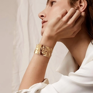 Detailed view of a wide gold open cuff bracelet with a hammered texture on a model's wrist