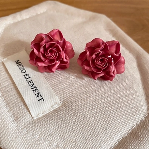 Detailed macro view of retro rose flower stud earrings on textured beige jewelry pouch