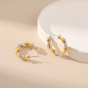 Macro detail of two-tone twisted C-shape earrings in gold and silver finish on ceramics