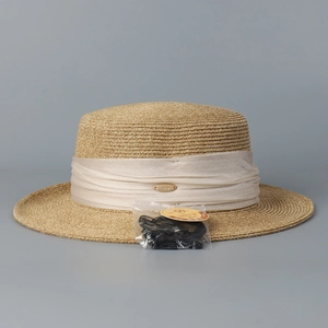 Détail d'un chapeau de paille beige avec ruban plissé, logo doré et étiquette protection UPF 50+
