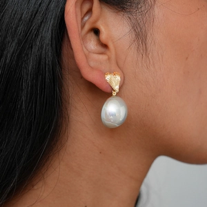 Detail of heart textured gold earring with a white baroque pearl on model side view