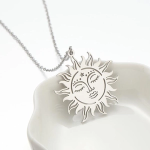 Close-up of silver hollow sun face pendant on a white ceramic tray detail