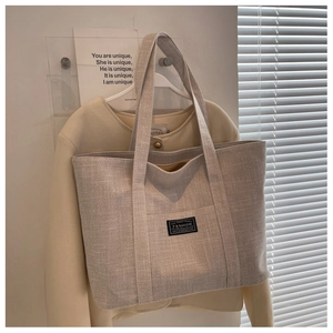 Detail of greyish beige tote bag with woven canvas texture and minimalistic labels