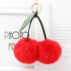 Close-up of fluffy red cherry keychain with green leaves and golden metal lobster clasp
