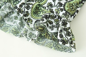 Close-up of textured paisley print fabric on a ruffled white and green bohemian blouse