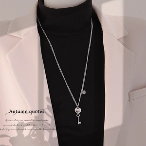 Silver heart and key pendant necklace styled on a model wearing an elegant beige blazer