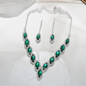 Macro detail of V-shaped necklace and drop earrings with green marquise-cut gems