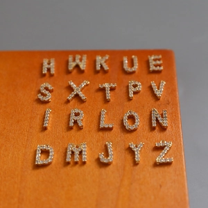 Close-up of 18k gold plated alphabet pendants with cubic zirconia on orange wood block