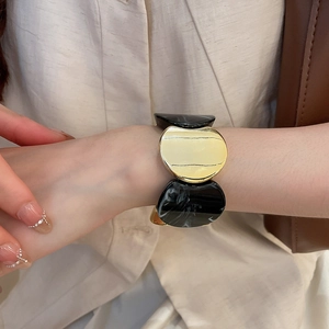 Détail d'un bracelet élastique avec maillons marbrés et métal doré porté au poignet