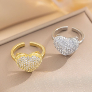 Adjustable gold and silver heart-shaped rings with zircon pavé settings on warm background