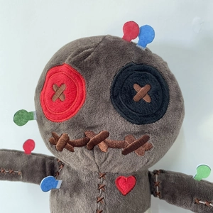 Brown plush voodoo doll with red heart embroidery and colorful pins on white background