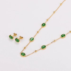 Macro detail of gold necklace and stud earrings set with oval green emerald stones