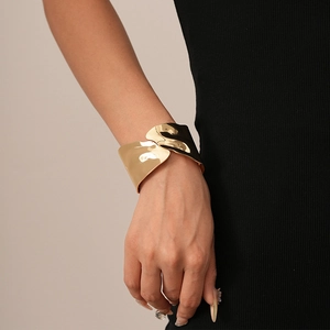 Close-up of a wide irregular golden cuff bracelet with wavy texture worn on a wrist