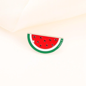 Close-up of cute watermelon enamel pin with vibrant red and green colors on beige fabric