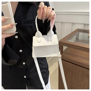 Detail einer weißen Mini-Quadrat-Handtasche mit goldenen Beschlägen und Tragegriff