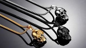 Three gothic skull necklaces in silver, gold, and black metal displayed with reflections