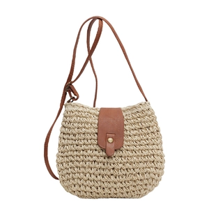 Borsa a tracolla in paglia intrecciata con cinturino in pelle marrone su sfondo bianco