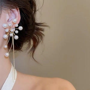 Detail view of large starburst drop earrings with pearls and tassels on a model