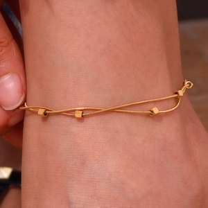 Detail of double-layered gold snake chain anklet with cubic beads on skin