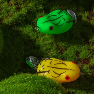 Macro view of green and yellow frog fishing lures with metal hooks on moss background