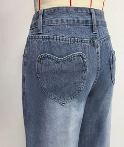 Detail of heart-shaped stitching on light blue washed denim back pocket of wide leg jeans