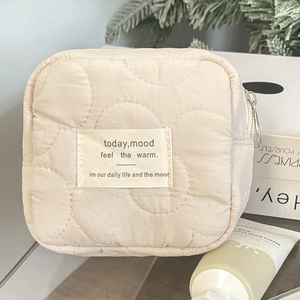 Close-up of cream quilted cosmetic bag with floral stitching and soft fabric texture