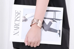 Close-up of rose gold cuff bracelet with wavy pattern worn by model holding a magazine